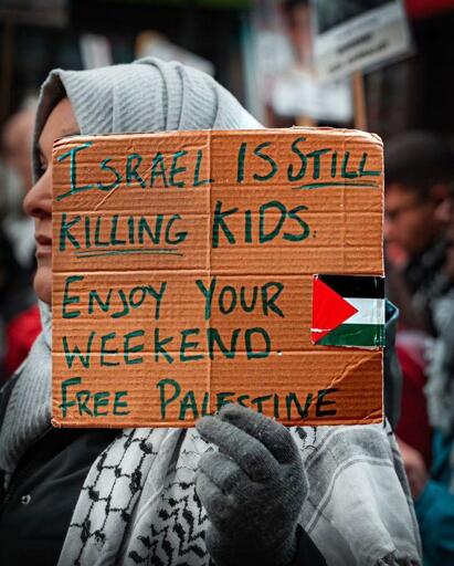 a woman holding a cardboard with the text"

ISRAEL IS STILL KILLING KID
ENJOY YOUR WEEKEND
FREE PALESTINE
